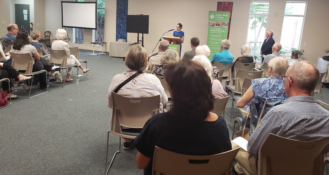 photo of Laura Dudas City Councillor speaking at the podium and the attendees of the event from the back