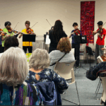 Members of Orkidstra play violin, viola, cello while volunteer attendees watch